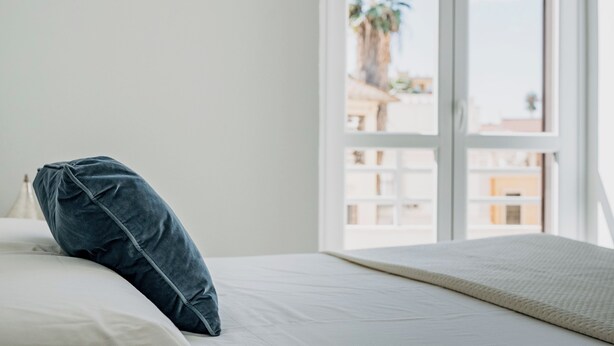 Ein Schlafzimmer mit Bett, Fenster und Blick auf Gebäude und Palmen.
