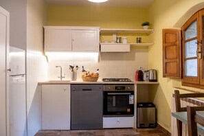 A compact kitchen with white cabinetry, a dishwasher, an oven, and a small trash bin.