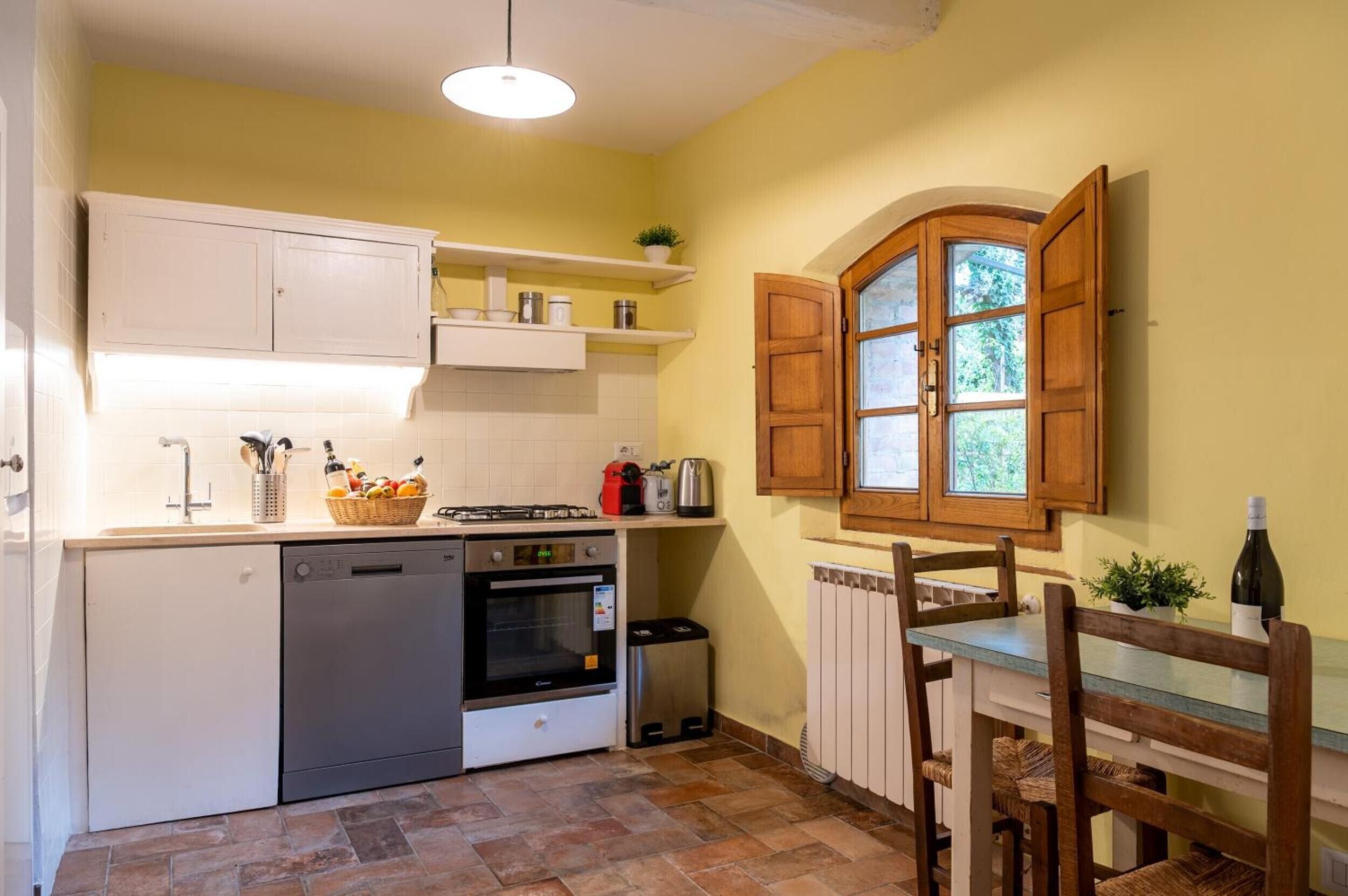 A compact kitchen with white cabinets, a built-in oven, a dishwasher, and a dining table with chairs.