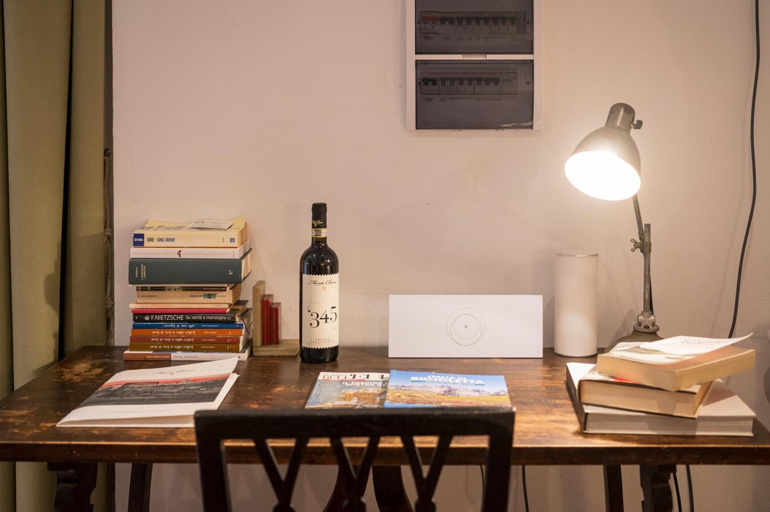 Een bureau met een laptop, een fles wijn, boeken en een bureaulamp.