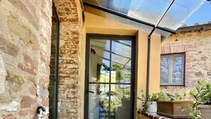 A narrow outdoor corridor with a glass door leading to a covered area, brick walls, and potted plants. - Apartment 'Tiziana' with Shared Garden and Wi-Fi (Vico dʼArbia)