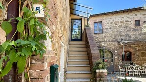 A stone building with a staircase leading to a door, outdoor seating, and greenery. - Apartment 'Tiziana' with Shared Garden and Wi-Fi (Vico dʼArbia)