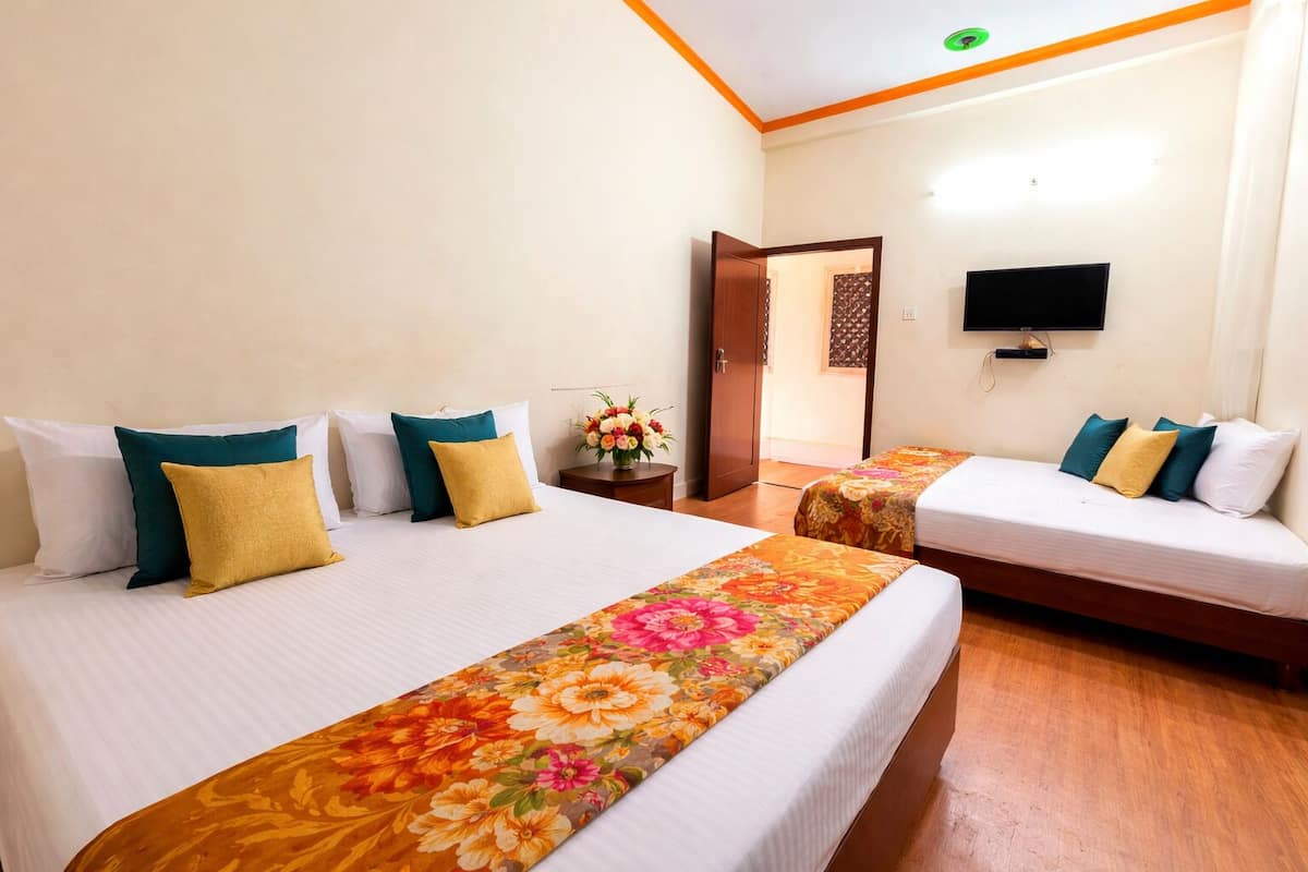 A hotel room with two beds, a TV, and a wooden floor.