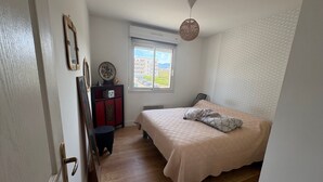 Een slaapkamer met een bed, een dressoir, een stoel, een raam en een hanglamp.