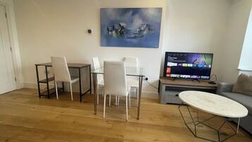 Uma sala de estar com área de jantar, um quadro na parede e uma TV exibindo a interface de um serviço de streaming.