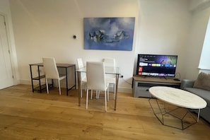 Una sala de estar con comedor, un cuadro en la pared y un televisor mostrando la interfaz de un servicio de streaming.