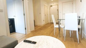 A modern living room with a round coffee table, a grey sofa, and a dining area with white chairs and a glass table. - Modern Flat/central Croydon/sleeps 4/free Parking (Croydon)