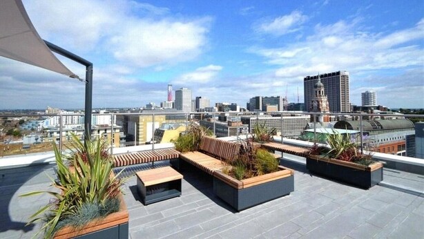 Terraza en la azotea con zonas de estar, macetas y vistas del horizonte urbano.