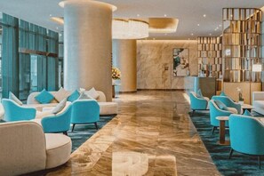 Eine Lobby mit Marmorboden, einer Sitzecke mit Sofas und Sesseln, einem Empfangstresen und einem Bücherregal.