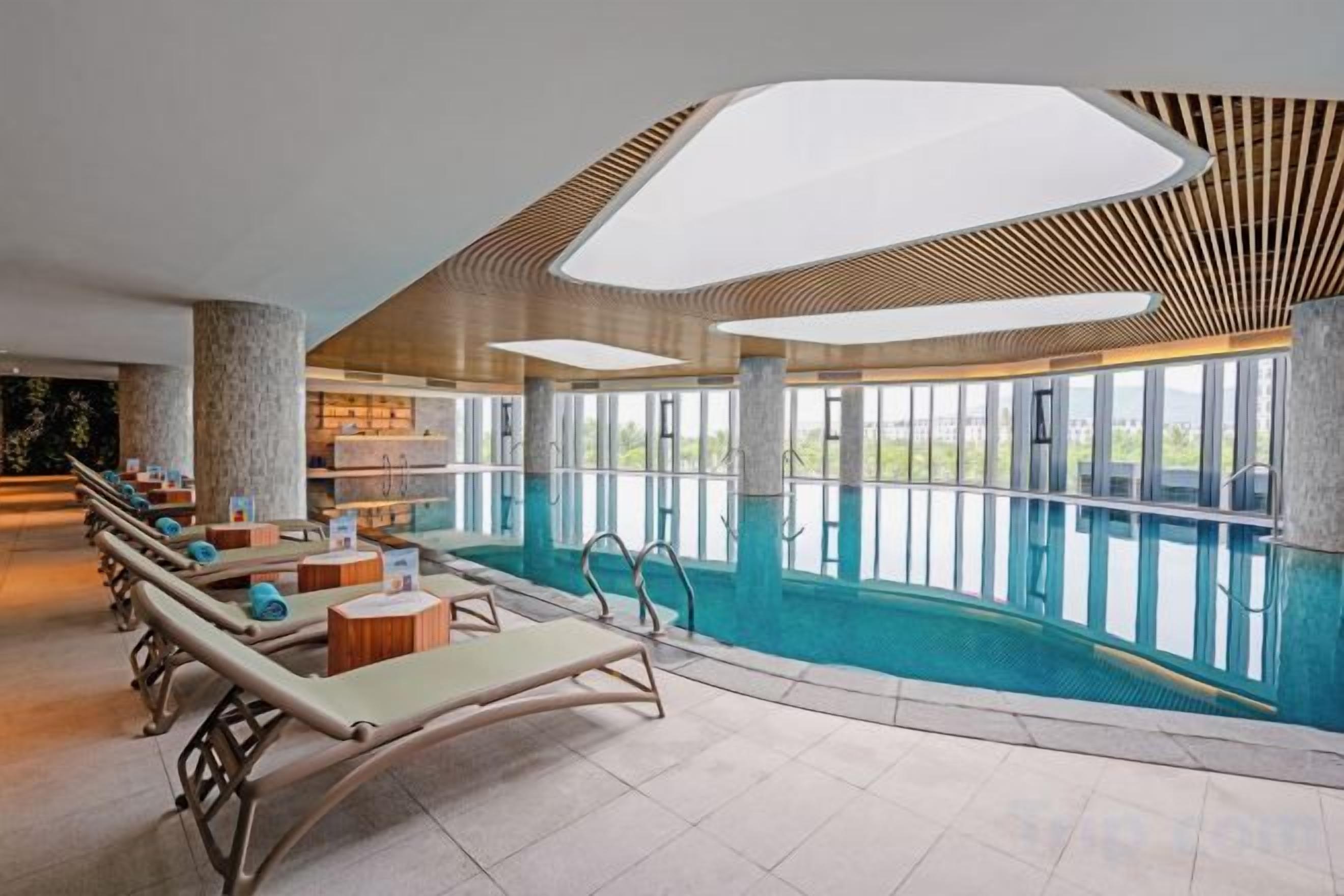 An indoor swimming pool with lounge chairs and a view of the outdoors.