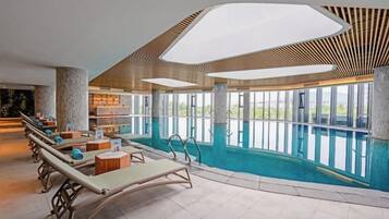An indoor swimming pool with lounge chairs and a view of the outdoors.