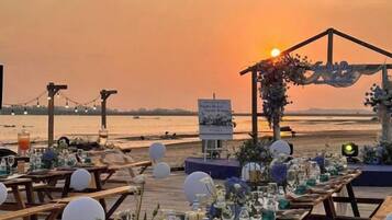 An outdoor wedding setup with a wooden deck, tables, and chairs, overlooking a body of water.