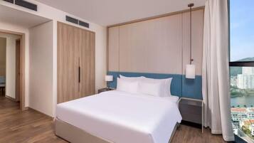 Ein Hotelzimmer mit einem großen Bett, einem Schrank, einem Nachttisch und Blick auf eine Stadtlandschaft durch ein Fenster.