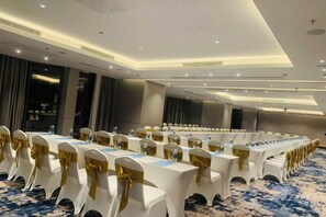 A conference room with rows of white tables, gold sashes, and blue carpeting. - Alacarte Halong Bay (Ha Long)