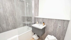 Un bagno moderno con cabina doccia in vetro, un lavandino bianco e un mobile contenitore grigio.