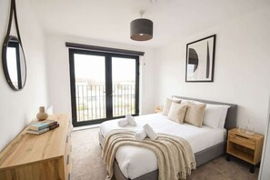 Quarto com cama, mesas de cabeceira, espelho, janela e porta.