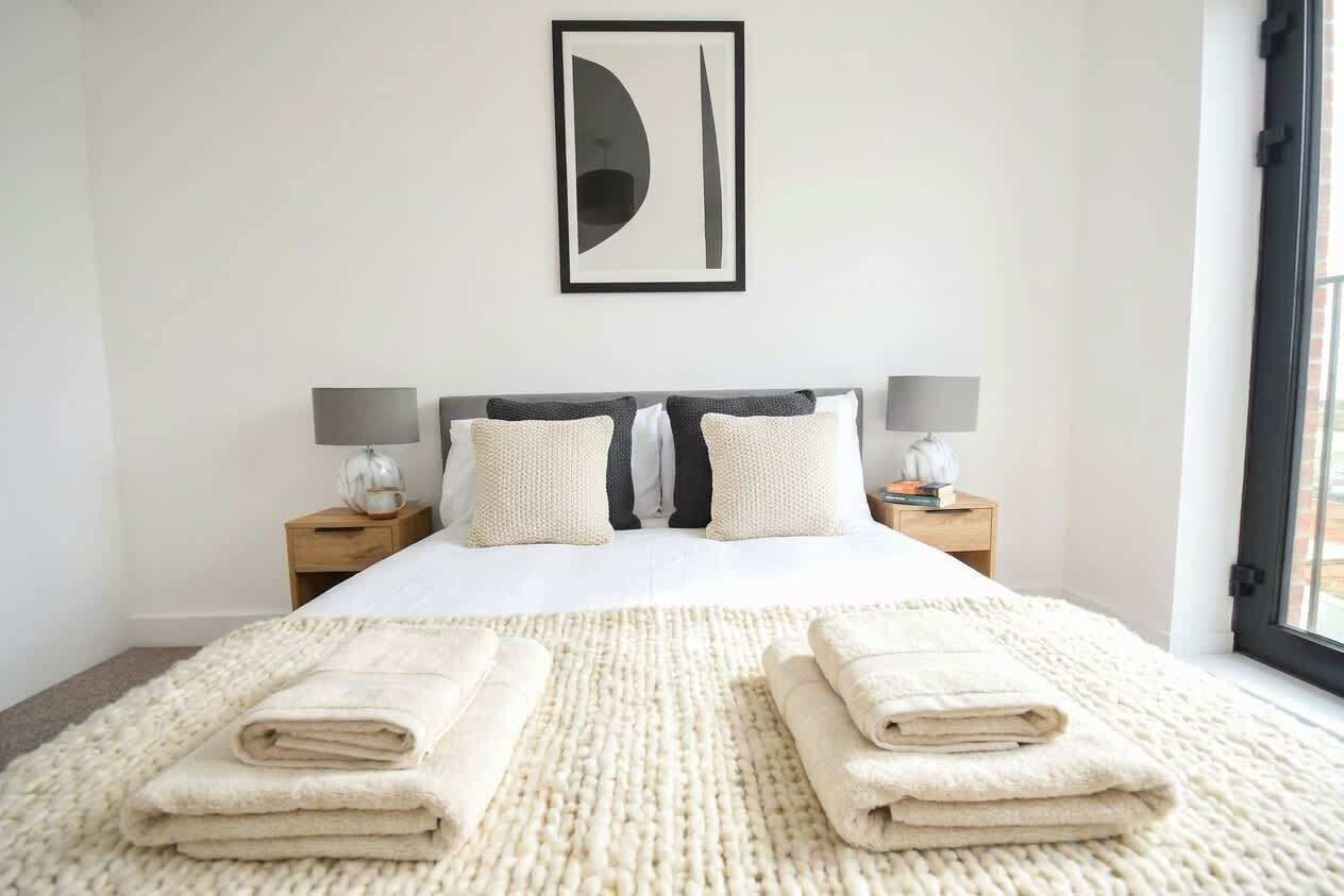 Ein Hotelzimmer mit einem Bett, zwei Nachttischen, einem großen abstrakten Gemälde und Blick durch das Fenster.