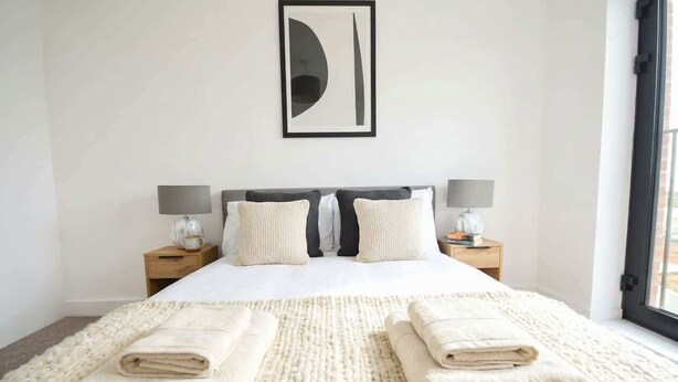 Una camera d'albergo con un letto, due comodini, un quadro astratto di grandi dimensioni e vista dalla finestra.