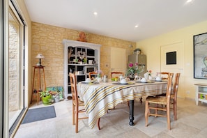 Un comedor con una mesa preparada para cuatro personas, rodeada de sillas de madera, una pared de piedra y una puerta.