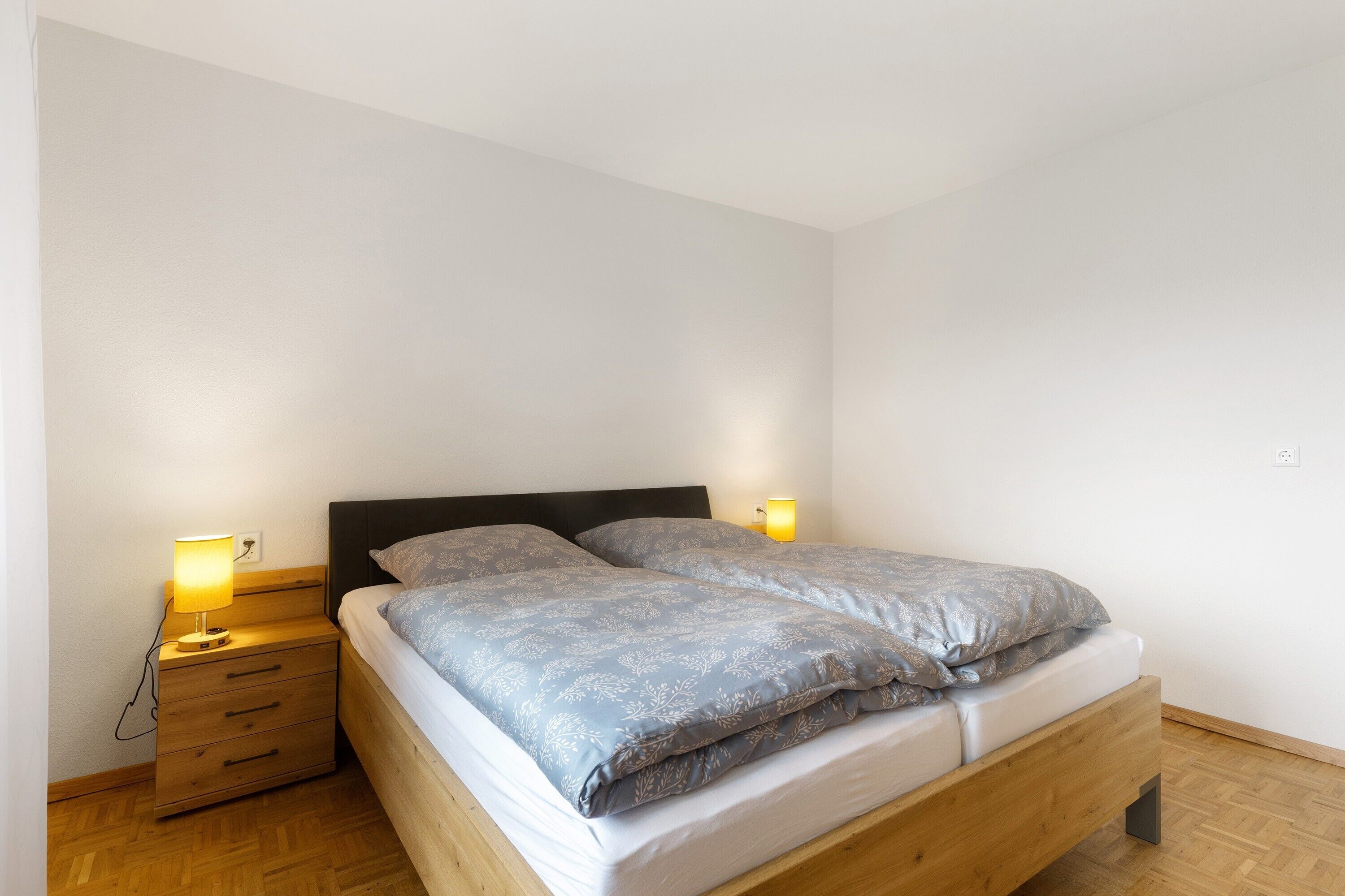 A single bed with a wooden frame, a nightstand with drawers, and two bedside lamps.