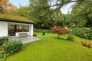 Een modern gebouw met een pannendak, een bankje buiten en een goed onderhouden tuin met verschillende struiken en bomen.