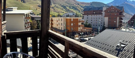 Un balcon avec vue sur une chaîne de montagnes, un bâtiment en bois et un espace de stationnement.
