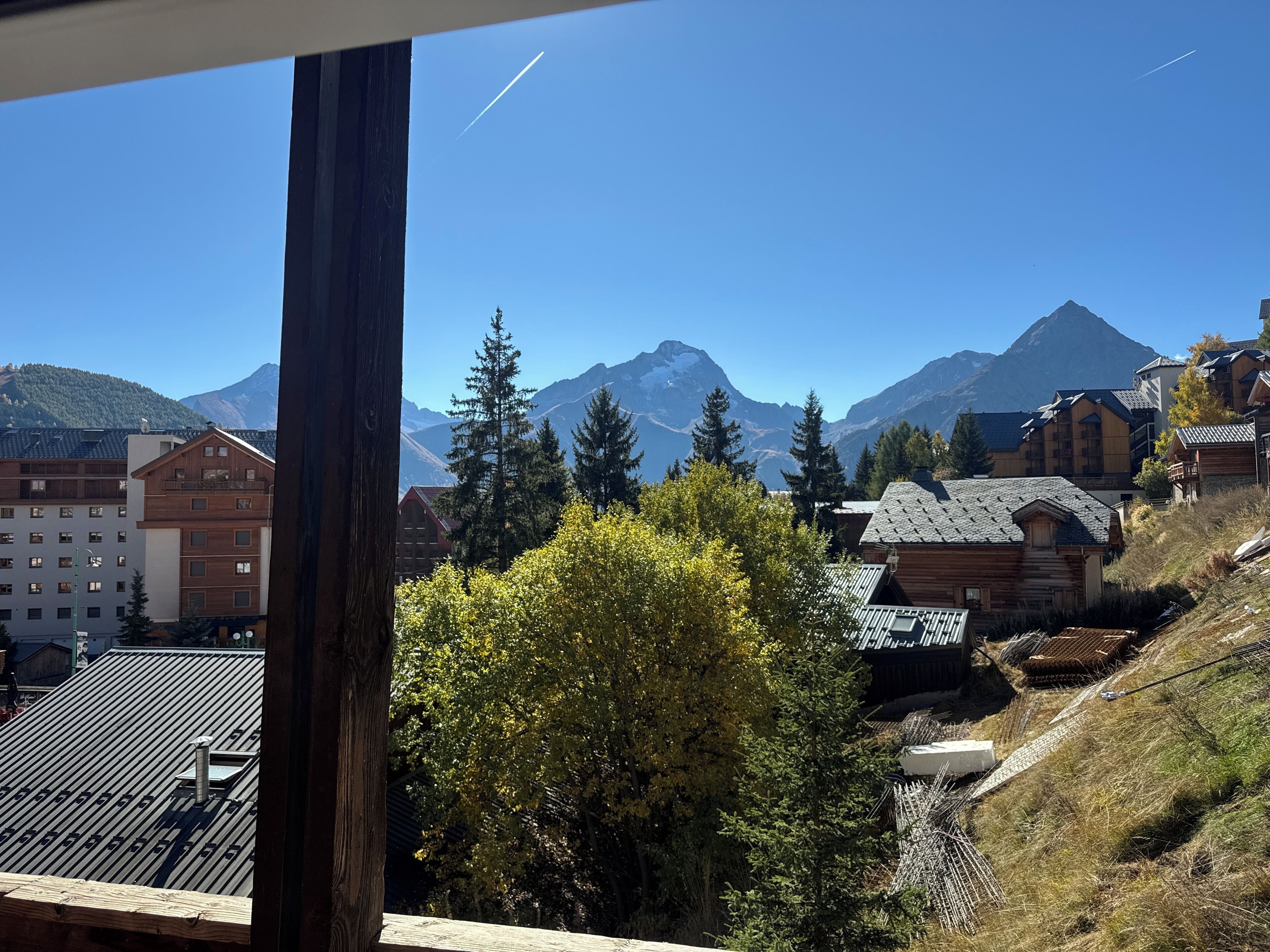 Un pueblo de montaña con edificios de madera tradicionales, vistas a montañas nevadas y un cielo azul despejado.