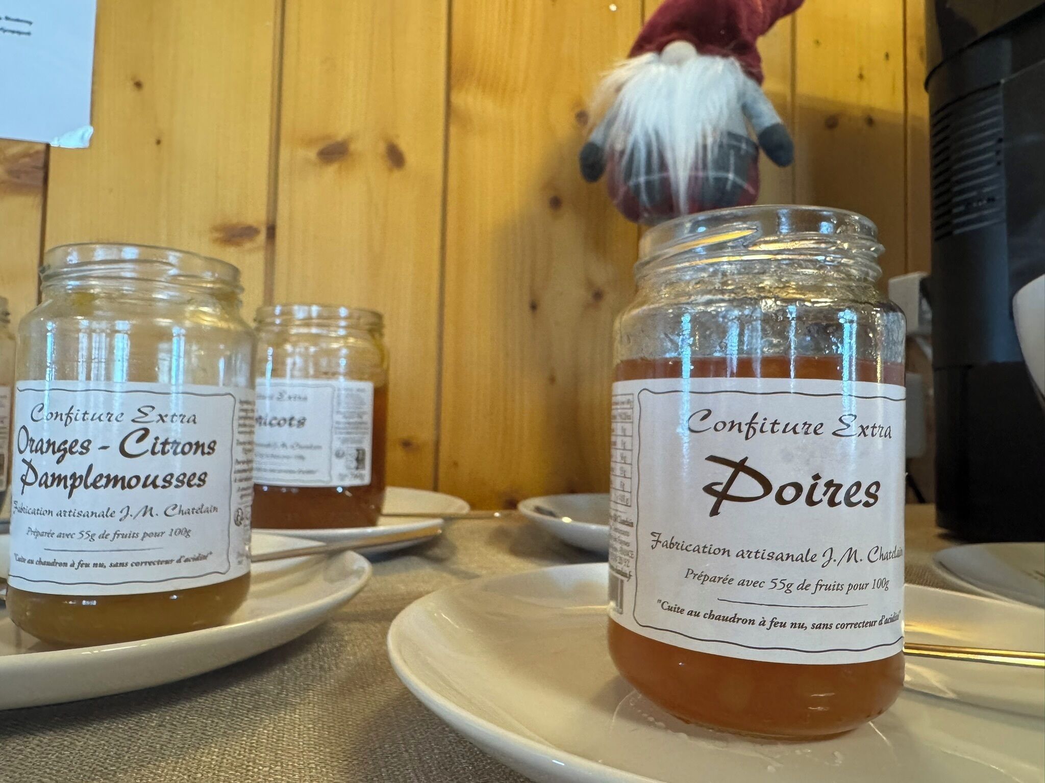 Drie glazen potten jam op witte borden, met etiketten waarop 'Confiture Extra' en 'Poires' staan.