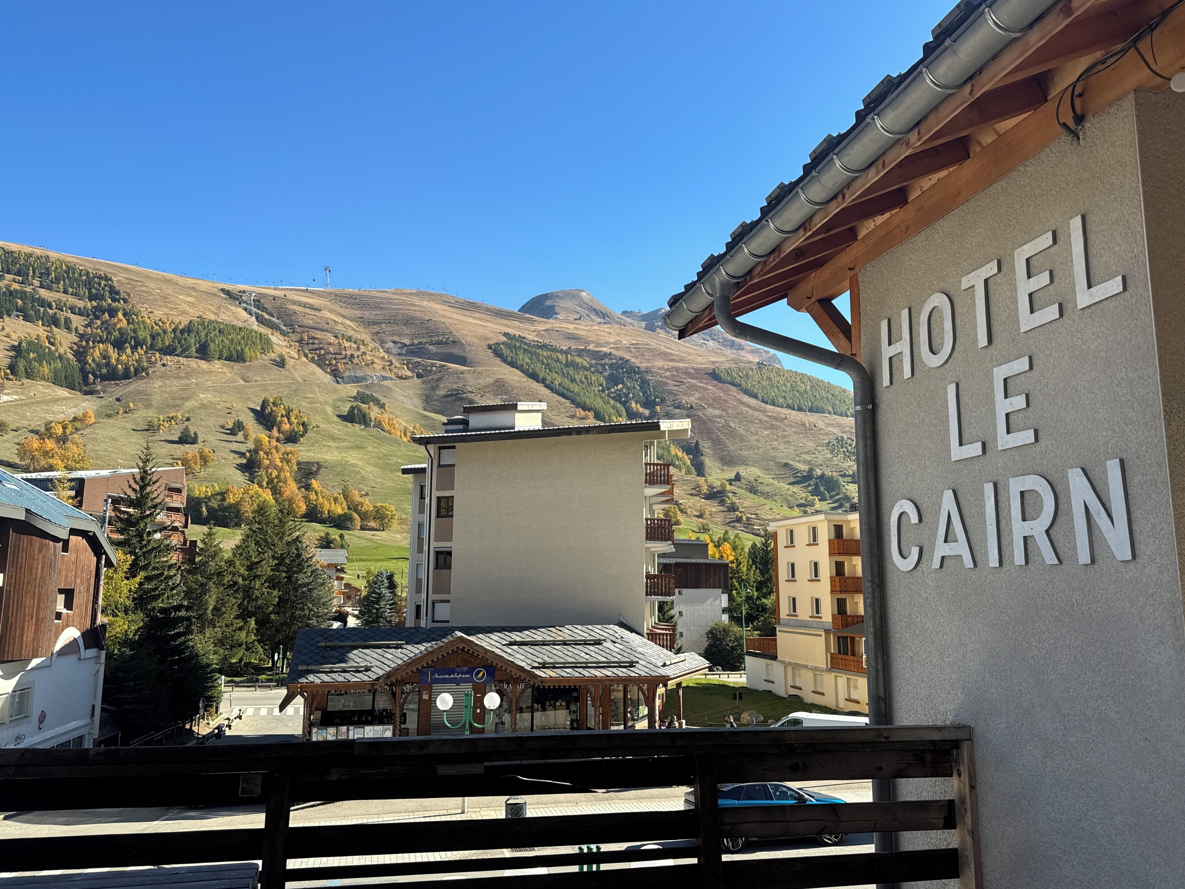 Un hotel llamado "HOTEL LE CAIRN" con vistas a montañas al fondo.