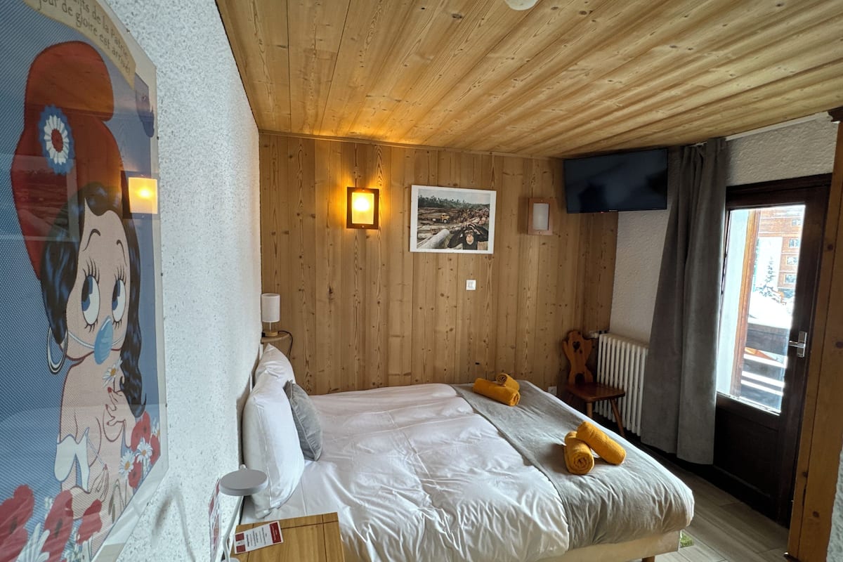 A bedroom with a wooden ceiling, a bed with white linens, a painting on the wall, and a window with curtains.