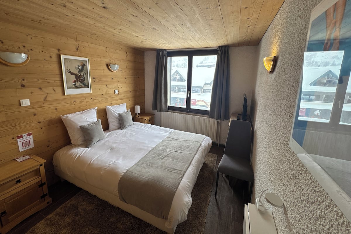 A wooden-paneled bedroom with a large bed, bedside tables, a chair, and a window with a view of buildings.