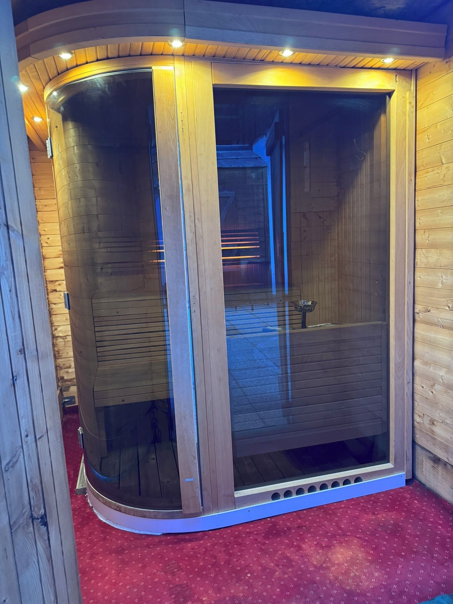 Una cabaña de madera con un vidrio que da a una habitación con alfombra roja.
