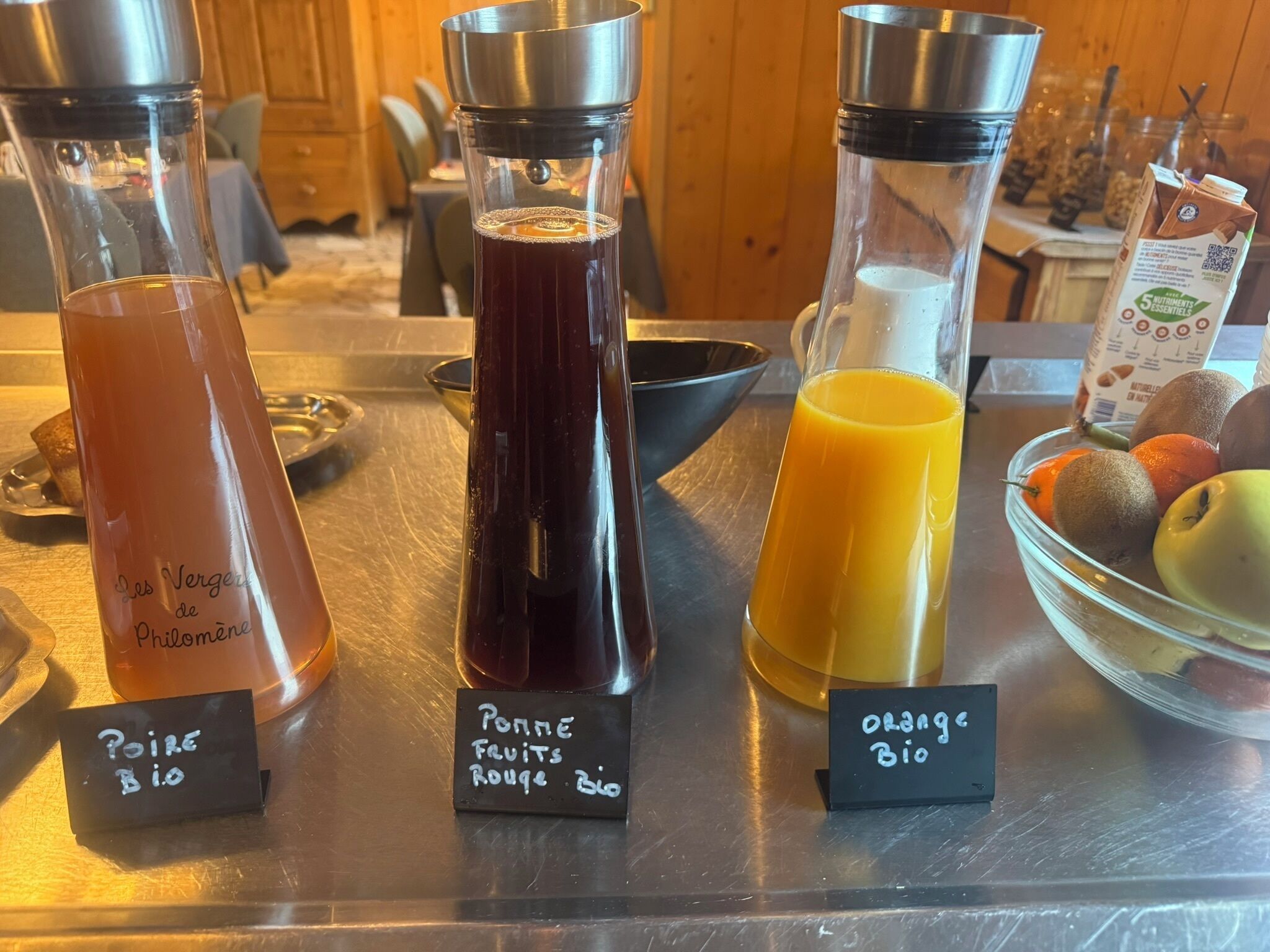 Una barra de zumos con tres dispensadores etiquetados: 'Pomme Bio', 'Pomme Fruits Rouge Bio' y 'Orange Bio'.