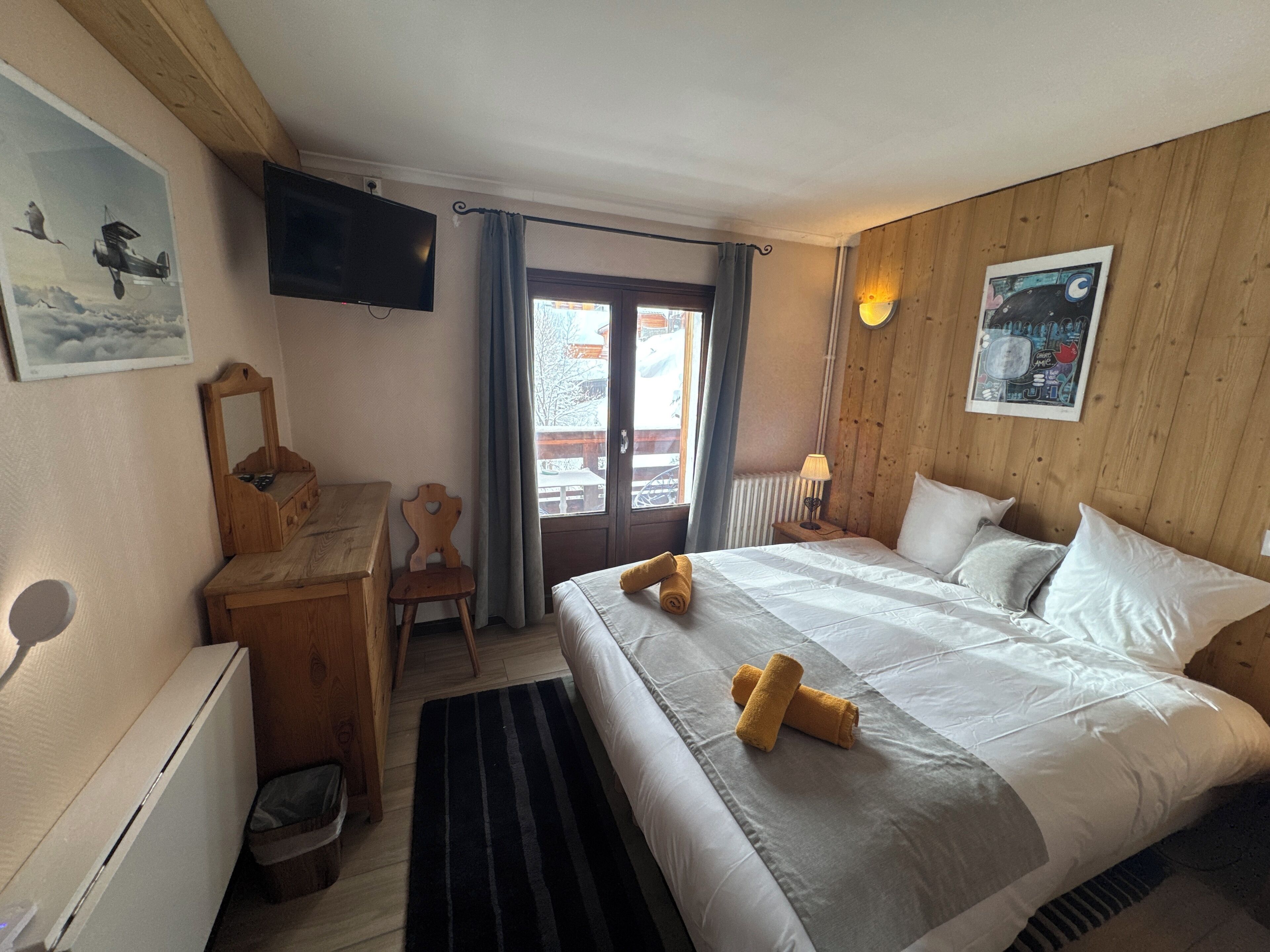 A hotel room with a bed, a desk, a chair, a television, and a window with curtains.
