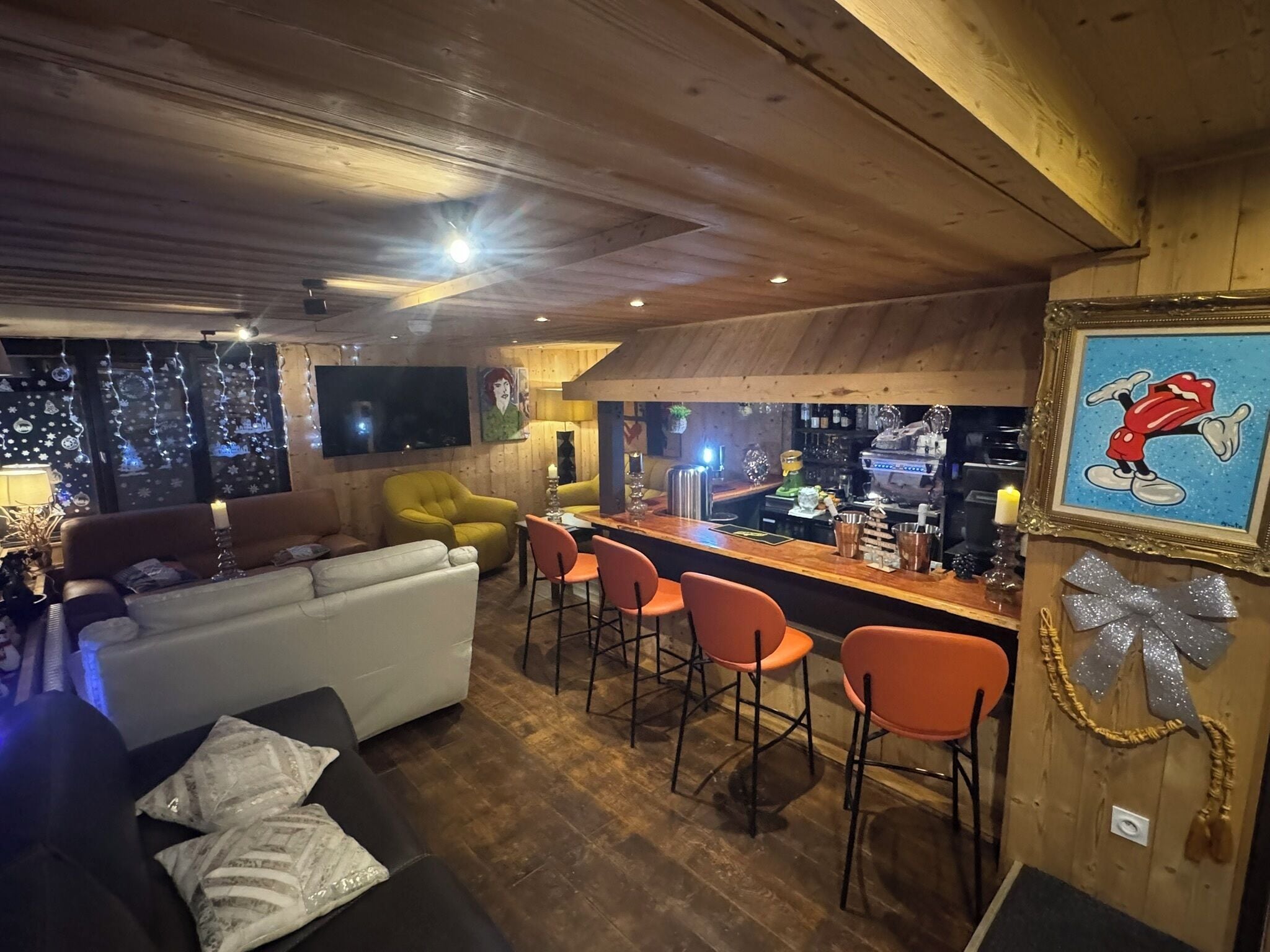 A cozy bar area with wooden walls, a bar counter, and orange bar stools.