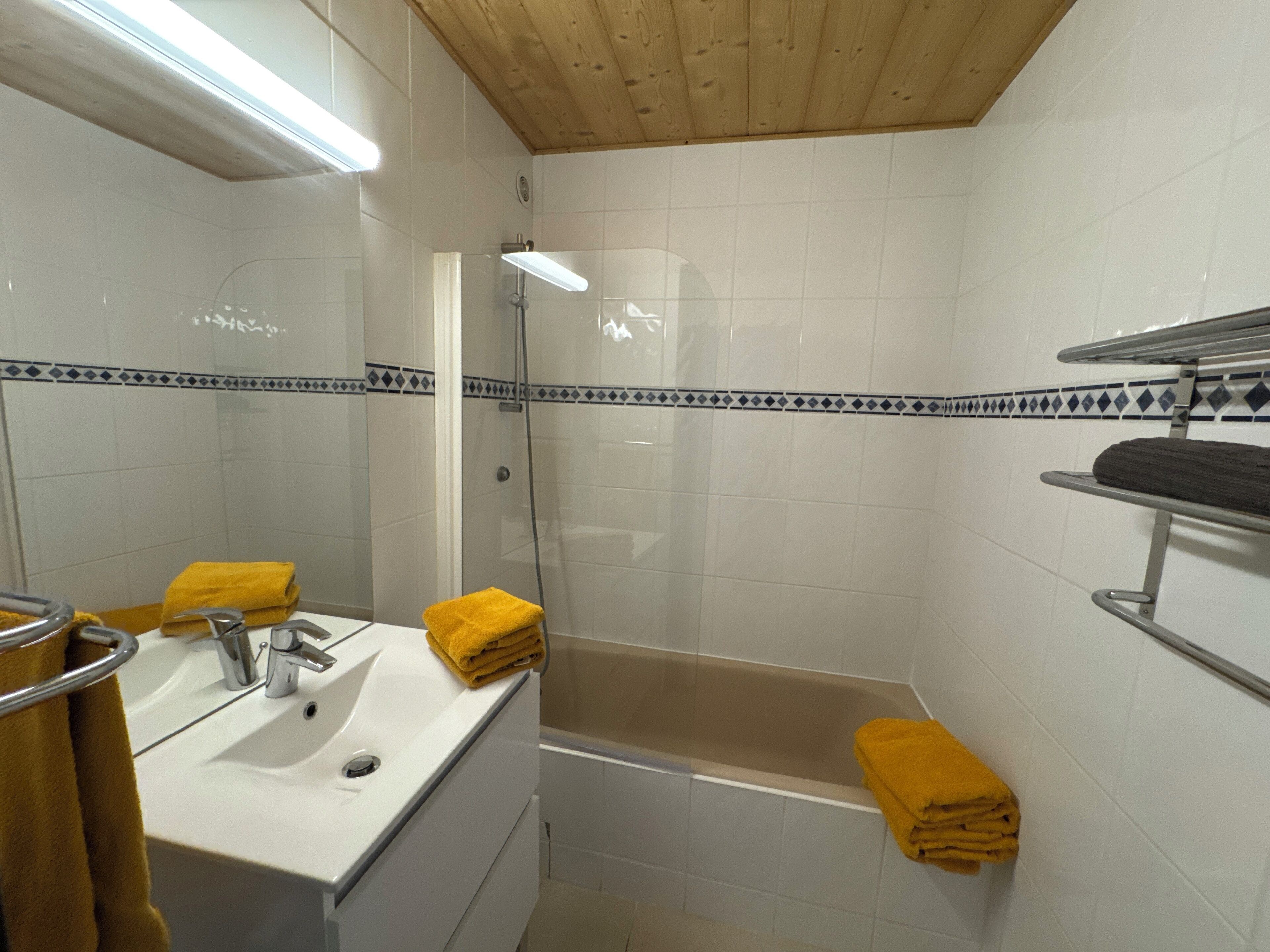 A bathroom with a bathtub, a sink, and a mirror. There are towels on the sink and the bathtub.