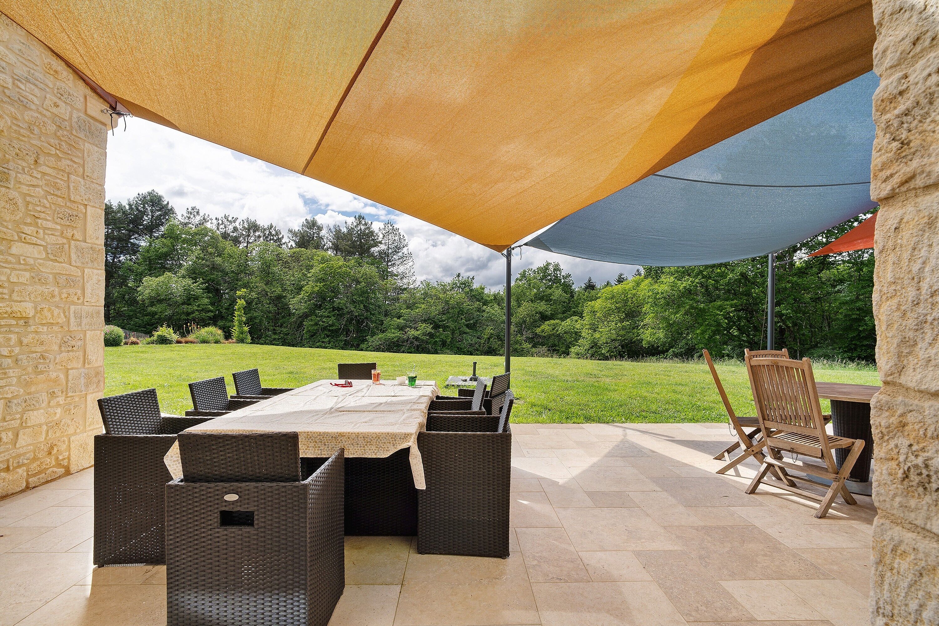 An outdoor patio with a table and chairs, a stone wall, and a grassy area in the background.