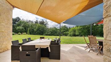 An outdoor patio with a table and chairs, a stone wall, and a grassy area in the background.
