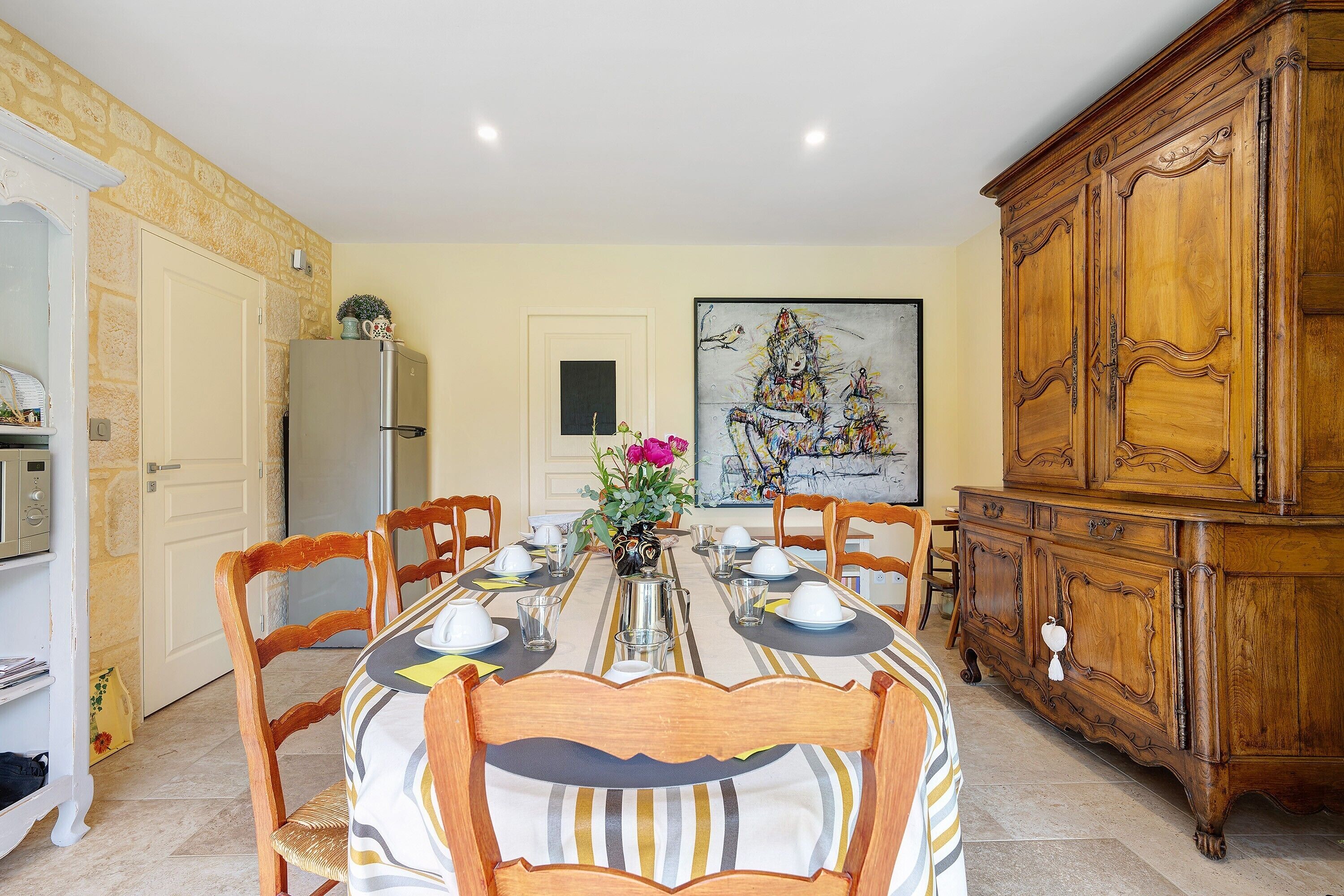 Un coin repas avec une table dressée pour quatre personnes, des chaises en bois, un buffet et un tableau accroché au mur.