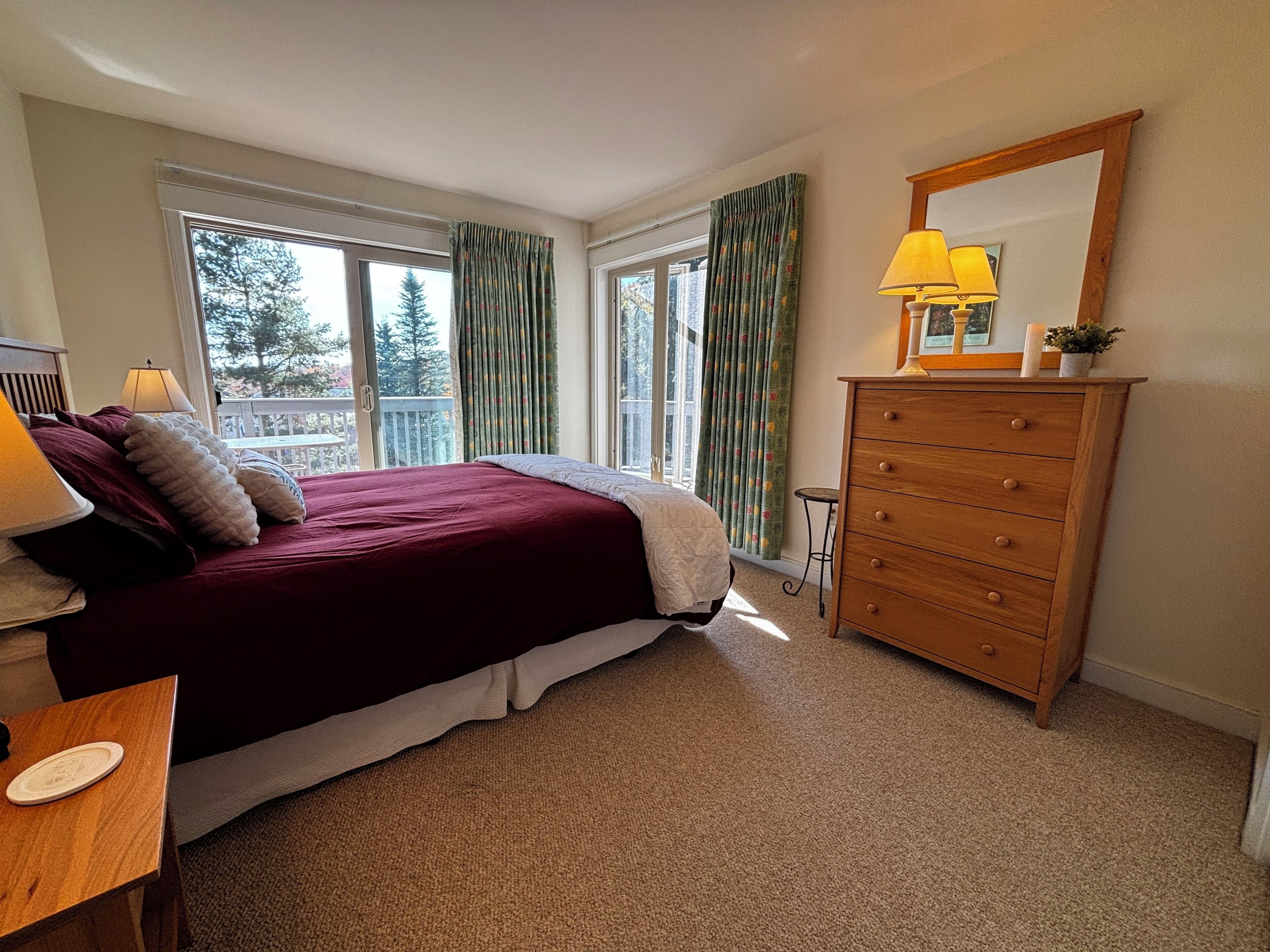 A bedroom with a bed, a dresser, a lamp, and a window with curtains.
