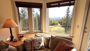 A cozy living room with a large window offering a view of a ski trail and mountains.