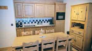 Une cuisine avec des meubles en bois, un dosseret carrelé, une table à manger avec des chaises et un four encastré.