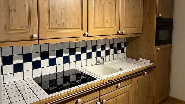 Une cuisine avec des meubles en bois, une plaque de cuisson noire et un dosseret carrelé.