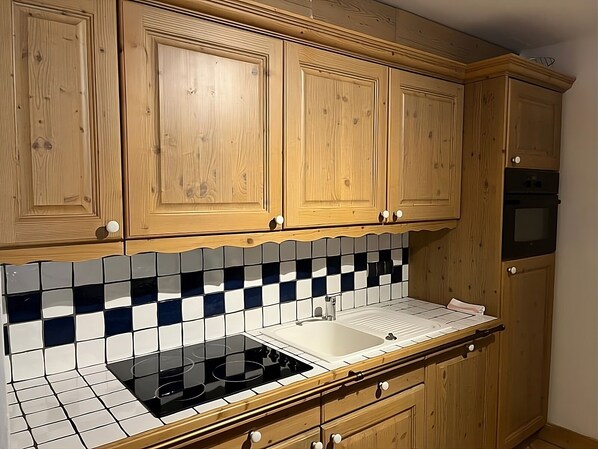 Une cuisine avec des meubles en bois, une plaque de cuisson noire et un dosseret carrelé.