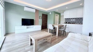 A modern living room with a TV, sofa, dining table, chairs, and a kitchen area. - The Bugibba Central Penthouse! (Saint Paul's Bay)