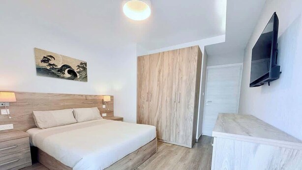 A bedroom with a bed, bedside table, wardrobe, and a TV mounted on the wall. - The Bugibba Central Penthouse! (Saint Paul's Bay)
