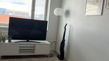 Un dormitorio con una cama, un televisor sobre un mueble bajo, un aspirador y una ventana con persianas.