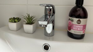 A bathroom sink with a modern faucet, a bottle of Cedarwood Rose Water, and two small potted plants. - Magnificent 1-bedroom apartment in Kouvola city centre (Kouvola)