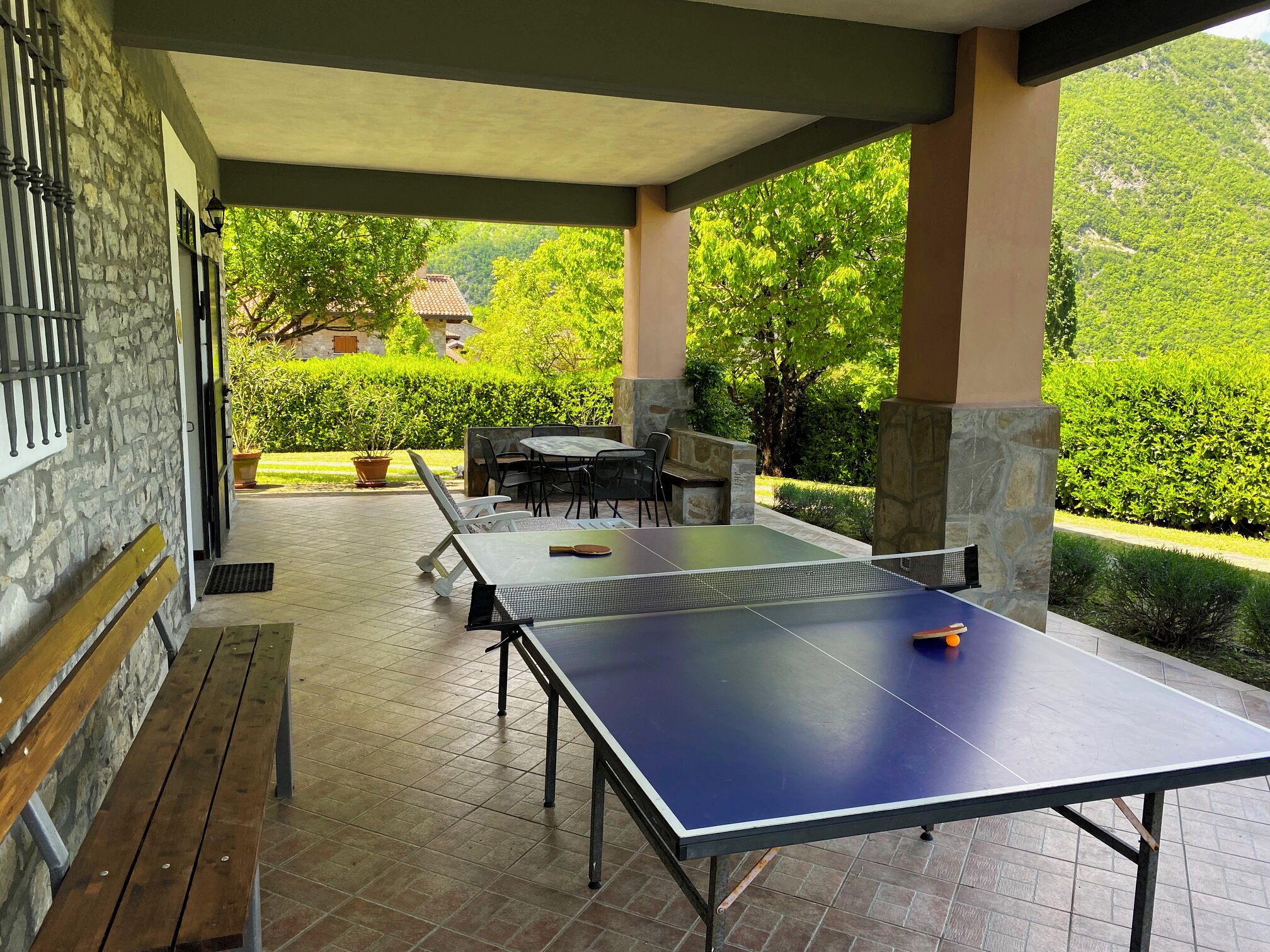 Un espace extérieur abrité comprenant une table de ping-pong, des sièges et une vue sur un jardin luxuriant et des collines lointaines.