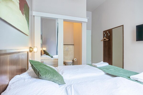 A hotel room with a bed, a mirror, a door, and a wall-mounted TV.